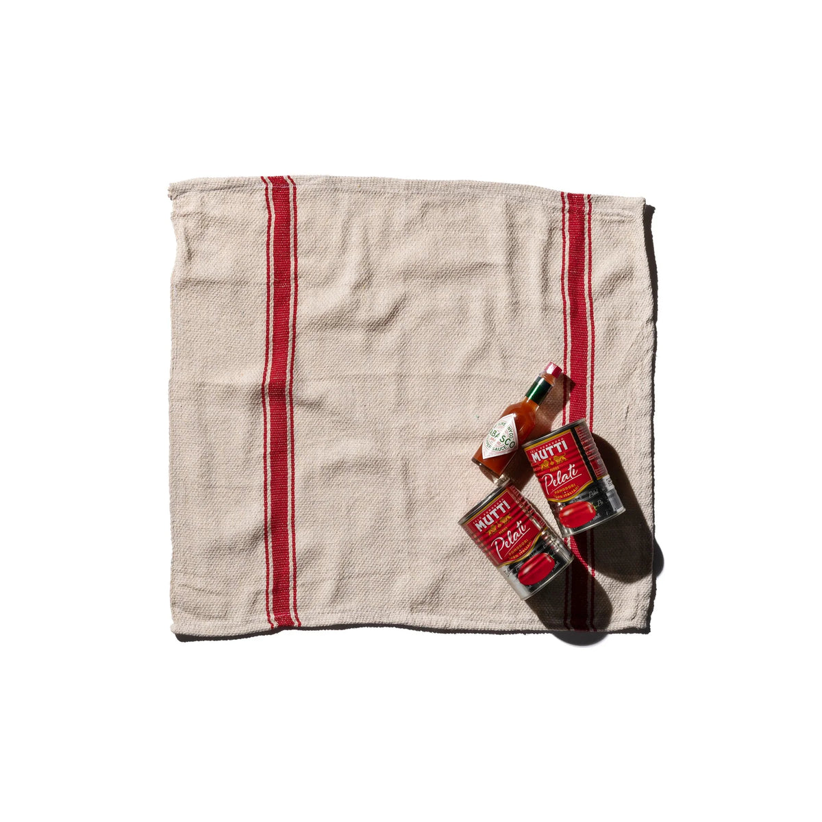 Een Puebco India Theedoek Rood 60/60, gemaakt van gerecycleerde stoffen, ligt plat op een witte achtergrond. Rechtsonder op het Puebco-doek staan twee flessen en twee blikjes tomatenproducten van Mutti.