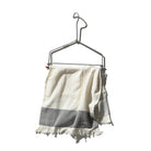 Een lichtgewicht witte handdoek met franjes en een grijze streep hangt aan de Keukenrolhouder Hanger van Puebco, met een minimalistisch ontwerp tegen een effen witte achtergrond.