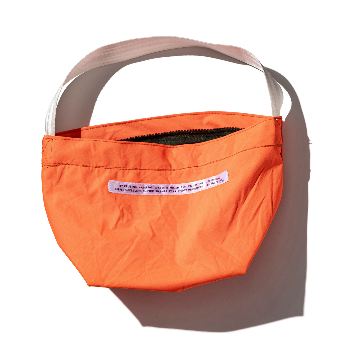 De Puebco Limited Edition Vintage Emergency Boat Tas van Puebco, gemaakt van gerecycled bootmateriaal in fel oranje, heeft een witte band en rits, een wit label met kleine tekst op de voorkant en steekt af tegen de witte achtergrond.
