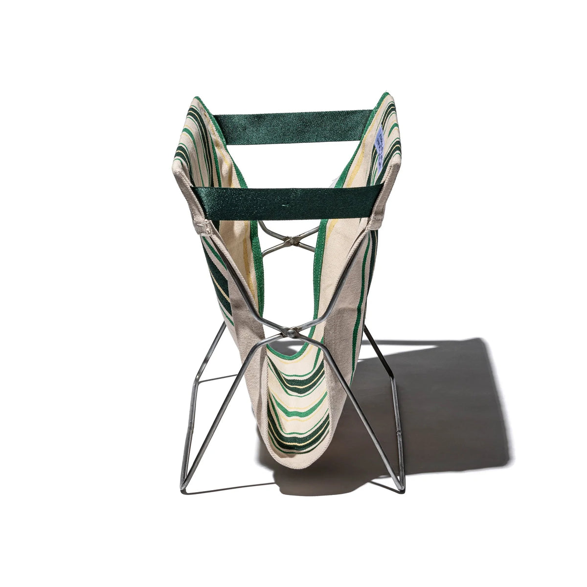 De Puebco Magazinehouder Café Groen Strepen heeft een modern, opvouwbaar ontwerp met een stevig frame en groen-beige gestreepte stof. Er wordt een schaduw geworpen op de witte achtergrond en er zit een opbergzak bij voor handig opbergen.