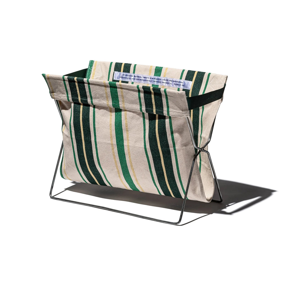 De Puebco Magazinehouder Café Groen Strepen heeft groene en gele verticale strepen op een stoffen opbergzak, geplaatst op een minimalistisch stalen frame en gefotografeerd tegen een witte achtergrond.