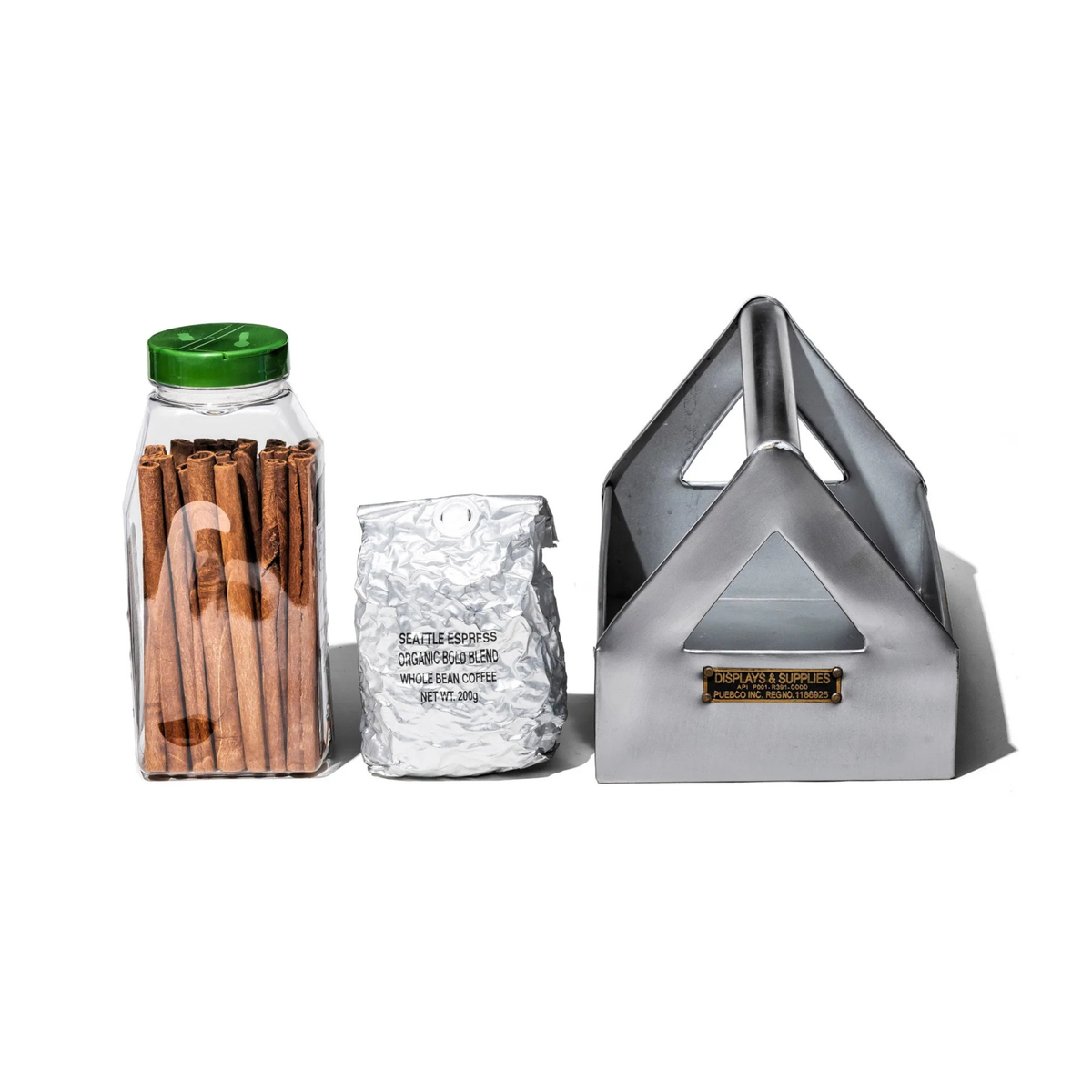 Een pot kaneelstokjes, een verzegelde zilveren koffiezak en een metalen servethouder staan netjes naast elkaar, als items opgeborgen in de Puebco Tool Organizer van Puebco op een witte achtergrond.