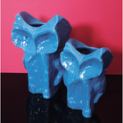 Twee glanzend blauwe Serax Marni After Midnight Uil Vaas Blauw S vazen met abstracte uilengezichten staan naast elkaar op een reflecterend zwart oppervlak, tegen een felroze achtergrond.