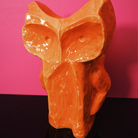 De Serax Marni After Midnight Uil Vaas Oranje S, een glanzend abstract oranje keramische uil sculptuur, wordt getoond tegen een roze en donkerpaarse achtergrond.