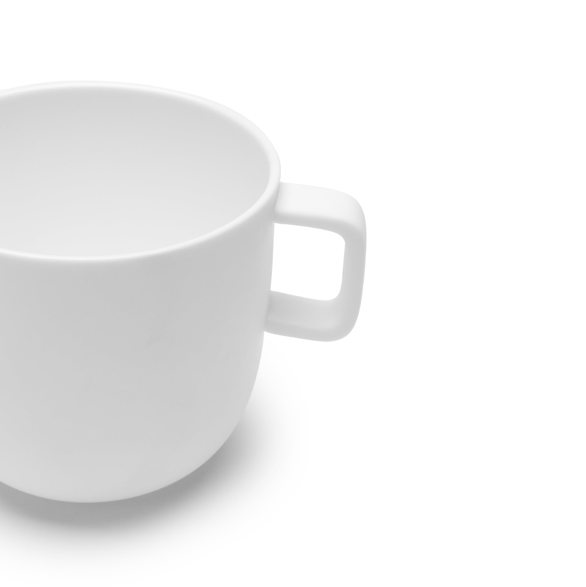 Een effen witte Serax Base Koffiekop met Oor 30 cl, een keramische koffiekop met een vierkant handvat, is gedeeltelijk zichtbaar op een witte achtergrond. De beker van Serax lijkt grotendeels leeg, met alleen de rechterhelft in beeld.