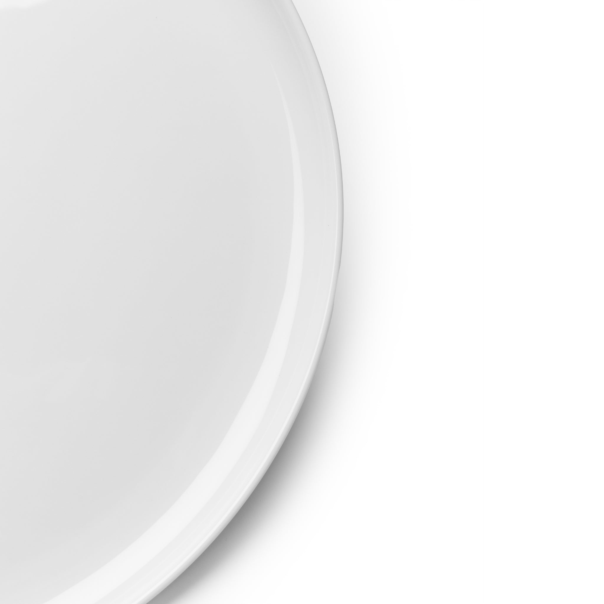 Een close-up van de Serax Base Laag Bord D24, een effen wit rond keramisch bord van Serax, toont alleen de linkerhelft van het bord tegen een witte achtergrond.
