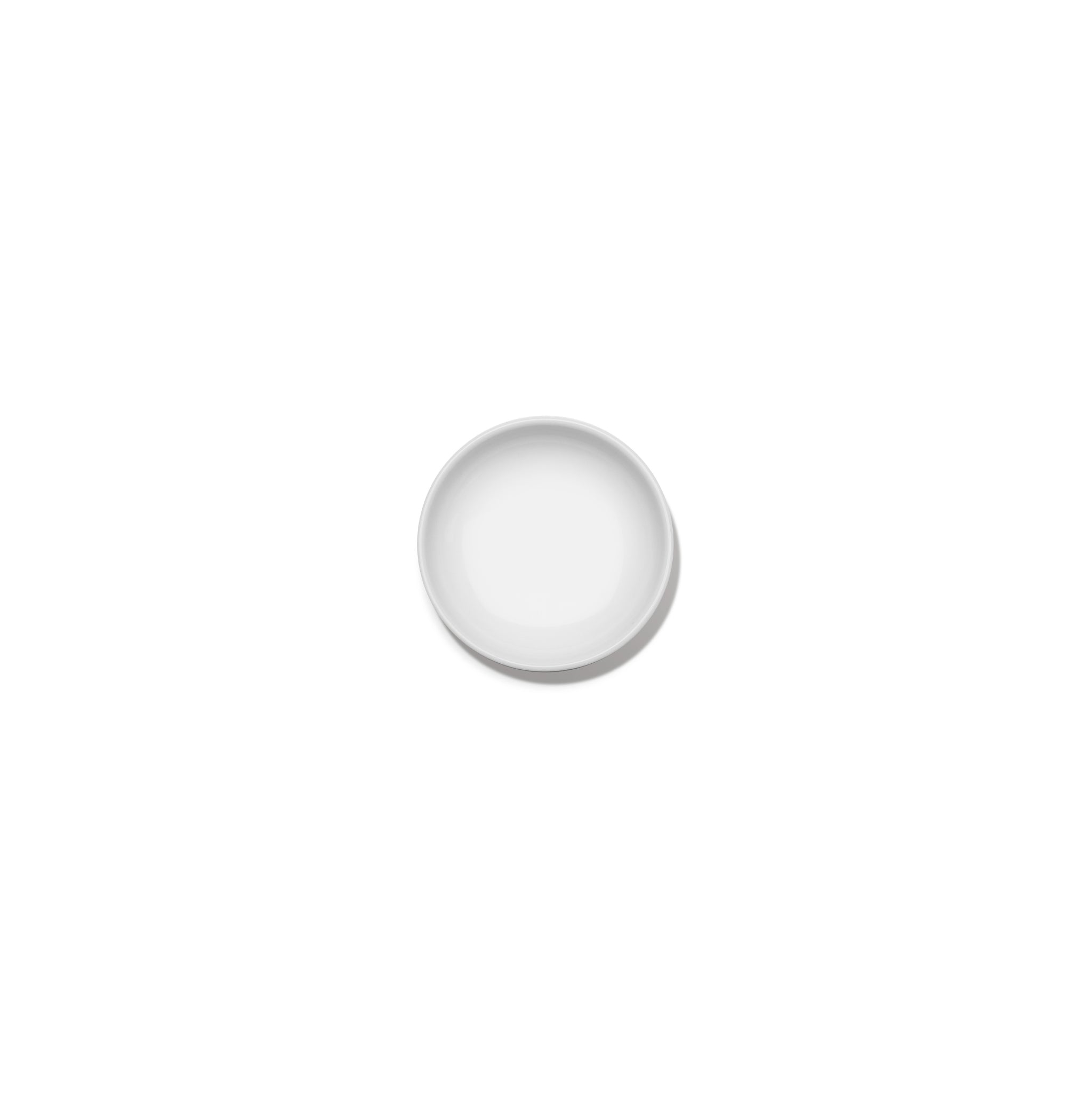 Een minimalistisch, klein, rond bord Serax Base Laag Bord D8 van Serax is gecentreerd op een effen witte achtergrond en van bovenaf bekeken. Het bord is leeg en heeft een elegant, eenvoudig ontwerp.