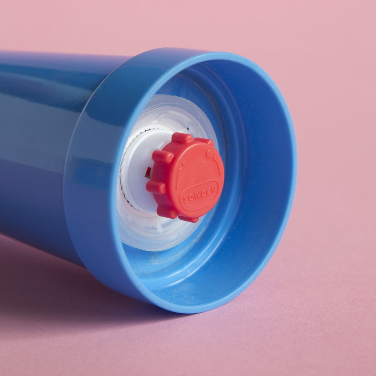 Een close-up van de blauwe Sowden Zout-en Pepermolen van Sowden, met een rode schroefdop en Memphis Design Movement inspiratie, rustend op een roze oppervlak.