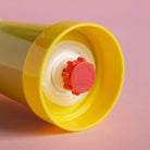 Een close-up van de gele dop en rode draaizegel van de Sowden Zout-en Pepermolen Geel van Sowden, tegen een roze achtergrond. Op de speelse rode zegel, geïnspireerd op de ontwerpen van George Sowden, staat "ZWEDEN" in reliëf.