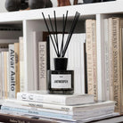 Een Wijck Diffuser Boulevard Antwerpen 200 ml van Wijck, met zwart riet, ligt bovenop een stapel boeken voor een boekenplank vol architectuur- en designtitels.