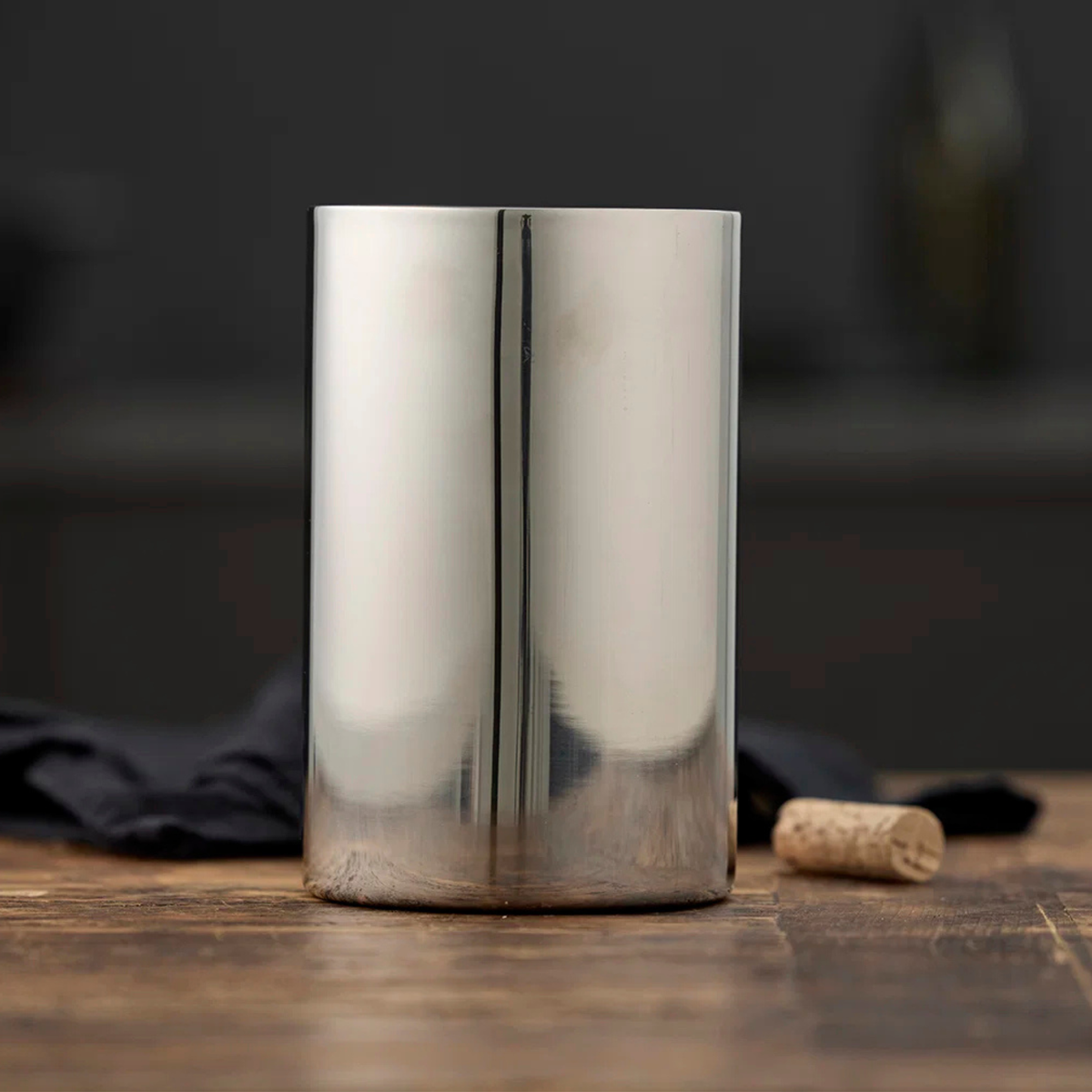 De Zone Denmark Funktion-wijnkoeler van Zone Denmark staat op een houten tafel naast een kurk en een donkere doek, tegen een donkere, wazige achtergrond.