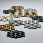 De Zone Denmark Triangles Trivet Rozemarijn heeft geometrische uitgesneden patronen in beige, grijs en wit, kunstig gerangschikt op een glad, lichtgekleurd oppervlak.