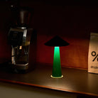 Een Fine Lumens Tipsy Lamp LED Oplaadbaar Zwart Emerald Groen werpt een gloed op een donker aanrecht naast een koffiemolen en een bruine papieren zak met het label "% ARABICA".