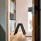 Een modern kantoor met houten vloeren, de Hasegawa Lucano Ladder 2 Step Zwart van Hasegawa in het midden, ingebouwde planken met kasten aan de linkerkant en een vergaderruimte op de achtergrond - allemaal subtiel geïnspireerd op Japans design.