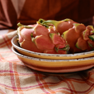 Twee roze, groen geschubde drakenvruchten rusten in een HK Living 70s Ceramics Curry Kom Hibiscus 2 st. kom op een geruite doek, met warme bruine en oranje tinten op de achtergrond.