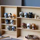 Op een houten plank staan kleine, ronde dierenfiguurtjes, waaronder katten, honden, een schaap en het Hoptimist Tijgerkat Oranje XS van Hoptimist - een ideale oranje decoratie of cadeau voor kattenliefhebbers. Dobbelstenen en garen rusten op de tafel vooraan.