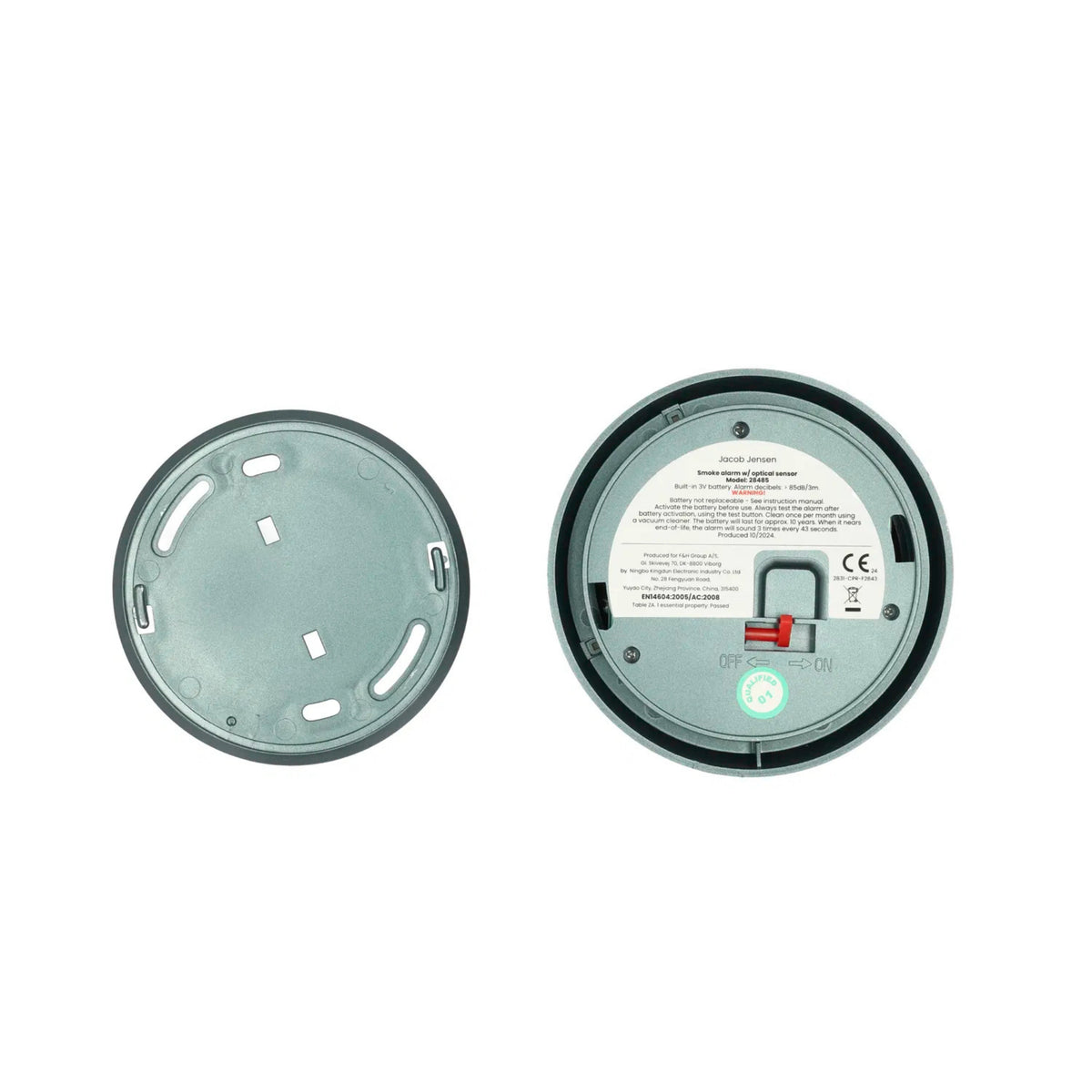 De Jacob Jensen Optical Rookmelder Groen D10 van Jacob Jensen heeft een grijs, cirkelvormig ontwerp waarvan het achterdeksel is verwijderd om het batterijvak, de rode schakelaar en het instructielabel te laten zien - een weerspiegeling van de Scandinavische stijl voor moderne interieurs.