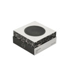 Een moderne vierkante doos toont een cirkelvormig zwart apparaat op het deksel, met het label Jacob Jensen Optical Rookmelder Zwart D10, een strakke zwart-witte rookmelder geïnspireerd op het minimalistische ontwerp van Jacob Jensen.