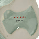 De basis van de Serax Marni After Midnight Uil Vaas Lichtblauw XS vaas van keramiek heeft een glanzend lichtblauw glazuur en op het ongeglazuurde gedeelte staat "MARNI" in rode en "SERAX" in zwarte letters.