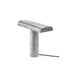 De Serax Fck Tafellamp Staal Grijs van Serax heeft een modern, minimalistisch ontwerp met een cilindrische basis, een platte rechthoekige metalen bovenkant en een zwart netsnoer, allemaal tegen een effen witte achtergrond.