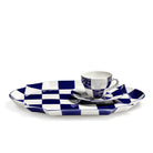 Op de Serax Wouters & Hendrix Fête Des Bêtes Dienblad Blauw Wit van Serax staan een witte porseleinen kop en schotel met een opvallend blauw-wit dambordpatroon tegen een effen witte achtergrond.
