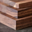Close-up van de hoeken van drie gestapelde Tareq Taylor Tarragon Snijplank Acacia A5 21/15 planken, die donker acaciahout laten zien met gladde, gepolijste oppervlakken en zichtbare natuurlijke nerfpatronen van Tareq Taylor.